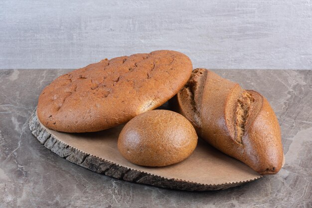 Assortimento di pagnotte di pane su una tavola di legno su fondo marmo. Foto di alta qualità