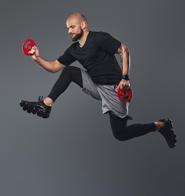 Atleta barbuto bello in abbigliamento sportivo che salta in uno studio. Isolato su sfondo grigio.