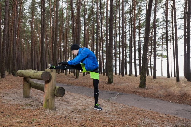 Atleta che allunga la gamba nella foresta