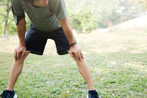 Atleta che riposa sul vetro verde nel parco al tramonto dopo aver eseguito con bottiglia di acqua (intensa luce solare e colore vintage).