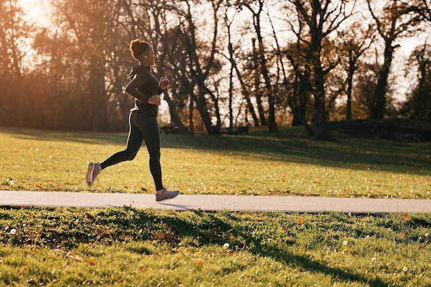 Atleta femminile afroamericano felice che corre nello spazio della copia del parco