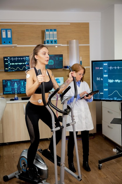 Atleta femminile che esegue i test sullo stepper e ha degli elettrodi su di esso e il medico segue sul suo tablet e monitora la sua evoluzione. Test clinici