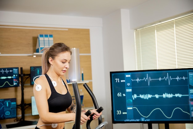 Atleta femminile che fa uno sforzo fisico sullo stepper e ha degli elettrodi attaccati e i risultati sono visualizzati sullo schermo. Laboratorio sportivo