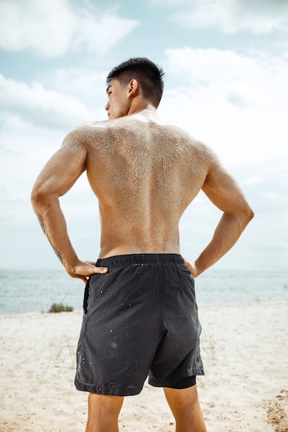 Atleta giovane uomo sano facendo squat in spiaggia