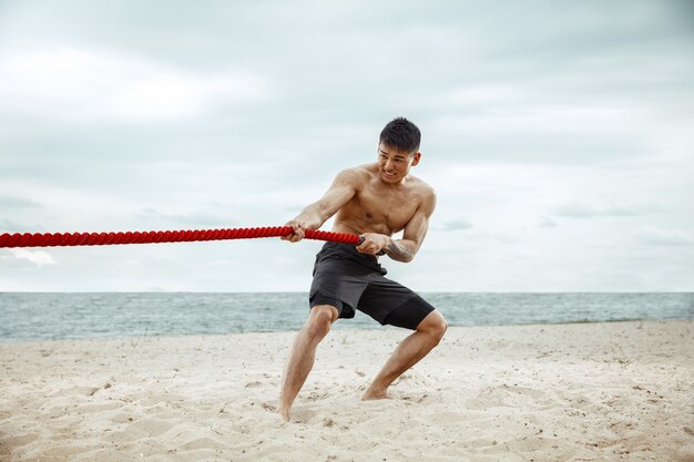 Atleta giovane uomo sano facendo squat in spiaggia