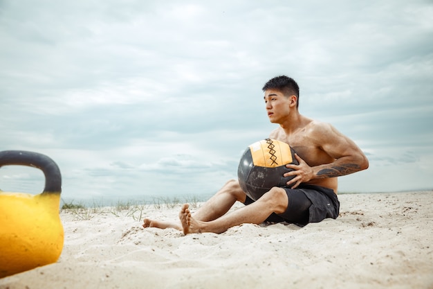 Atleta giovane uomo sano facendo squat in spiaggia