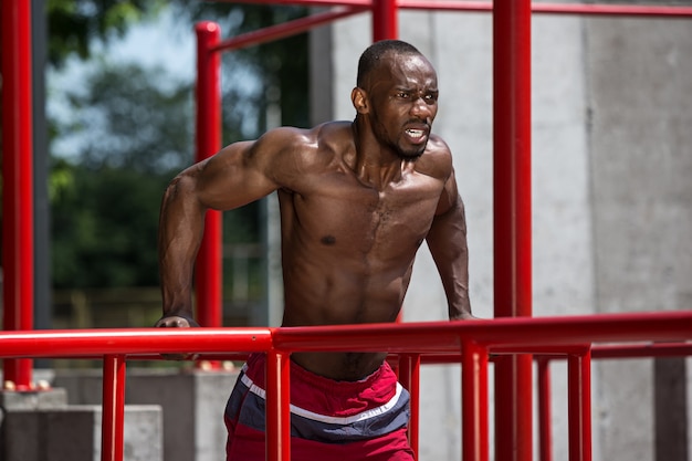 atleta in forma facendo esercizi allo stadio. Uomo afro all'aperto in città. Tirare su esercizi sportivi. fitness, salute, concetto di stile di vita