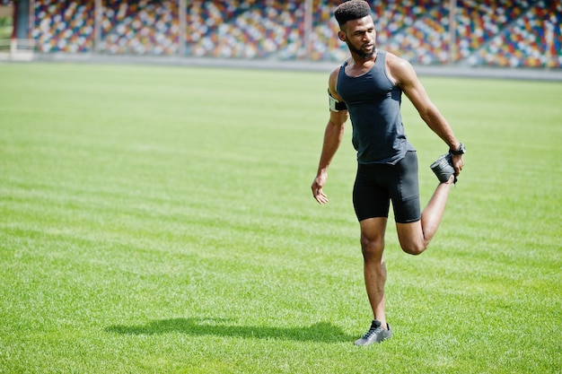 Atleta maschio afroamericano in abbigliamento sportivo che fa esercizio di stretching allo stadio