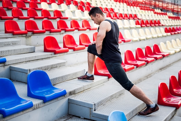 Atleta maschio che allunga la sua gamba sulla scala vicino alle gradinate