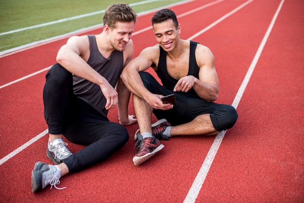 Atleta maschio che mostra qualcosa sul telefono cellulare ai suoi amici che si siedono sulla pista di corsa