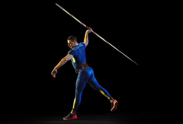 Atleta maschio che pratica nel lancio del giavellotto isolato su studio nero in luce al neon