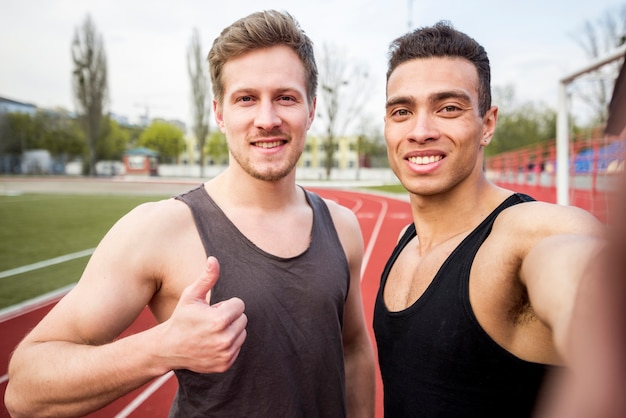 Atleta maschio sorridente due sulla pista di corsa che prende selfie sul telefono cellulare