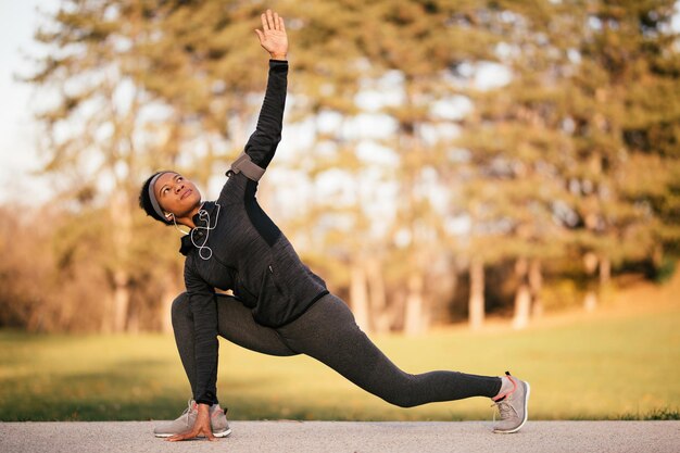 Atleta nera che si riscalda prima dei porti di allenamento e fa esercizi di stretching nel parco