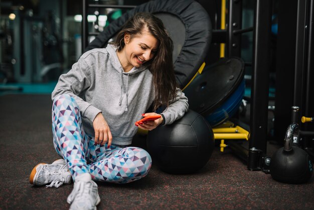 Atletica donna sorridente con smartphone in palestra