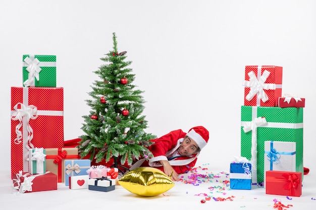 Atmosfera natalizia con Babbo Natale sdraiato dietro l'albero di Natale vicino a regali in diversi colori su sfondo bianco