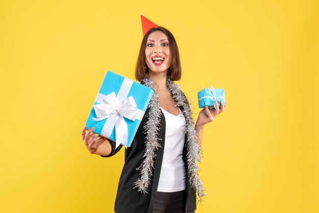 Atmosfera natalizia con donna d'affari orgogliosa in tuta con cappello di Natale che mostra il suo regalo su giallo