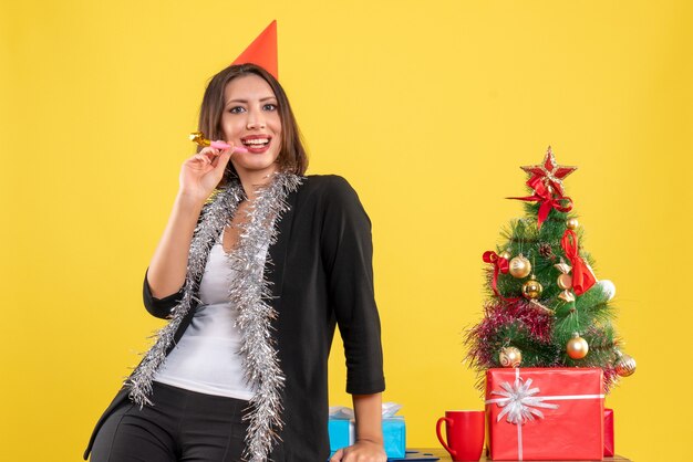 Atmosfera natalizia con sorridente bella signora in posa per la fotocamera in ufficio su giallo