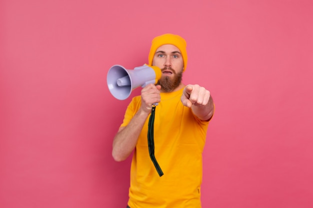 Attenzione! Uomo europeo con il megafono che punta il dito alla telecamera su sfondo rosa