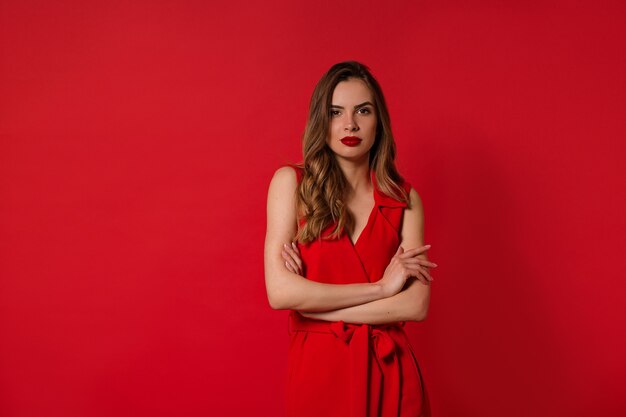 Attraente bella donna alla moda con i capelli ondulati che indossa un abito rosso con rossetto rosso