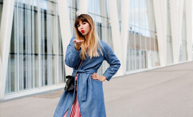 Attraente bella donna in cappotto blu in posa su edifici moderni