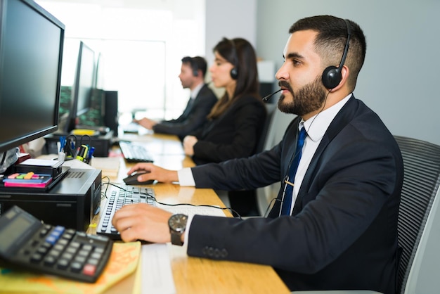 Attraente dirigente latino che offre servizio clienti con un auricolare e offre supporto tecnico in un call center affollato