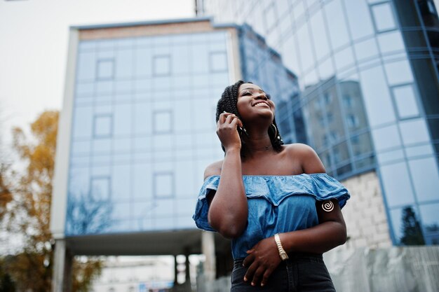Attraente donna afroamericana con dreadlocks in jeans indossano poste contro un moderno edificio a più piani