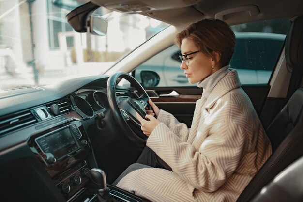 Attraente donna alla moda che si siede in macchina vestita di cappotto