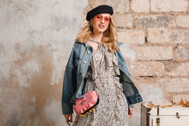 Attraente donna bionda alla moda in jeans e giacca oversize che cammina contro il muro in strada