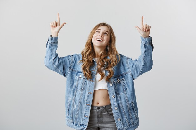Attraente donna bionda che punta le dita fino a copyspace, mostrando la pubblicità con un sorriso felice