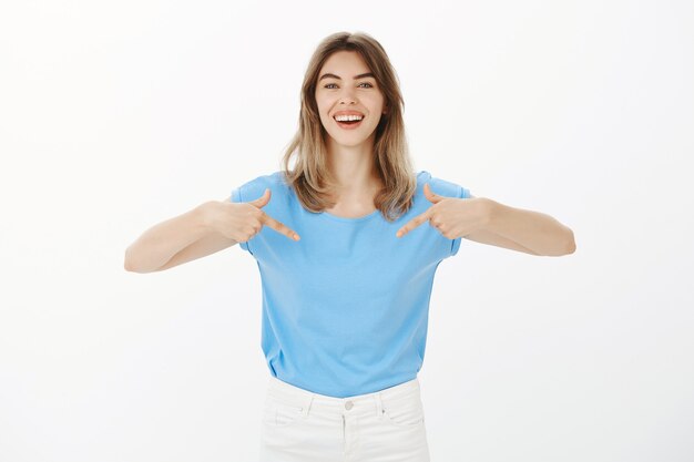 Attraente donna bionda felice che punta al tuo logo, mostrando banner aziendale