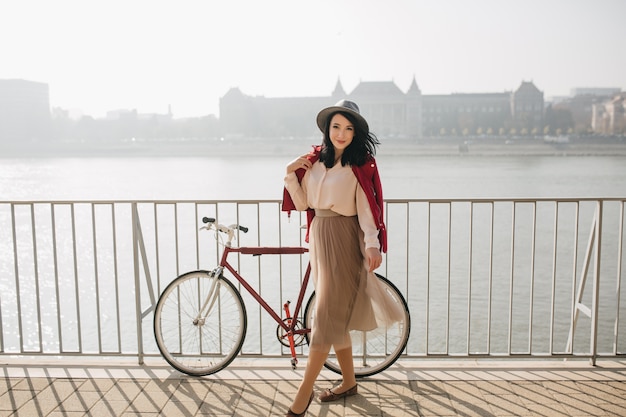 Attraente donna dai capelli corti in piedi sull'argine con la bicicletta