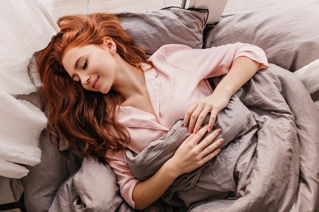 Attraente donna dai capelli lunghi che dorme mattina. Ragazza ispirata allo zenzero sdraiata a letto.