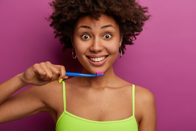 Attraente donna dai capelli ricci ha un sorriso sano a trentadue denti, tiene lo spazzolino da denti