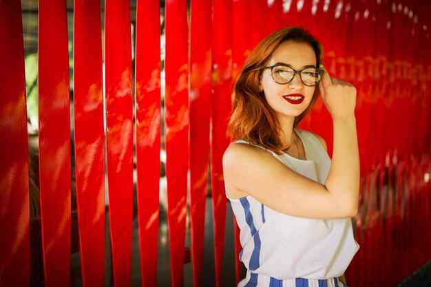 Attraente donna dai capelli rossi in occhiali in posa su sfondo rosso