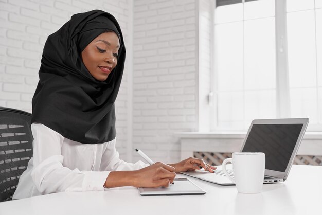 Attraente donna musulmana in hijab nero tramite computer