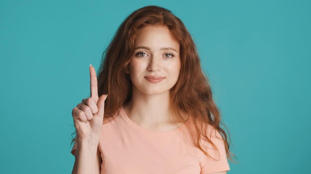 Attraente donna rossa che mostra il dito indice sulla fotocamera su sfondo colorato