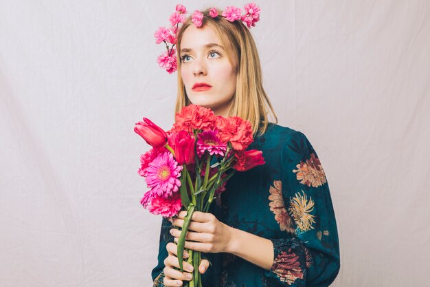 Attraente donna sensuale sognante con corona sulla testa e bouquet di fiori