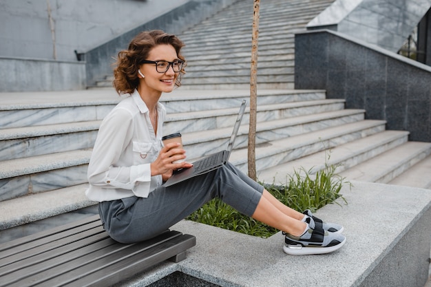 Attraente donna sorridente alla moda con gli occhiali che lavora digitando sul laptop