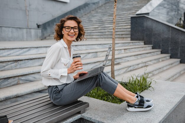 Attraente donna sorridente alla moda con gli occhiali che lavora digitando sul laptop