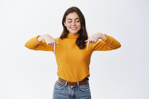 Attraente donna sorridente che punta e guarda il logo che mostra un banner pubblicitario su uno spazio vuoto in piedi in abiti casual su sfondo bianco