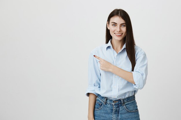 Attraente donna sorridente in camicia che punta il dito a sinistra