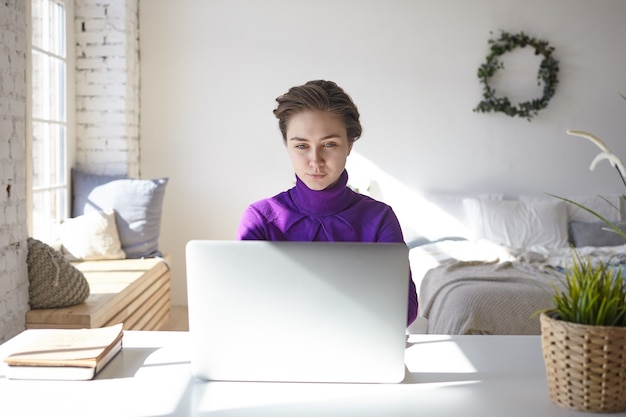 Attraente e concentrata giovane donna libera professionista che naviga nei siti web di reclutamento di lavoro, pubblicando il suo curriculum, alla ricerca di nuovi progetti e clienti