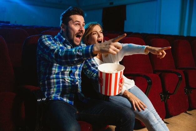 Attraente giovane coppia caucasica guardando un film in un cinema, casa o cinema. Guarda espressivo, stupito ed emotivo. Seduto da solo e divertendosi. Relazione, amore, famiglia, tempo del fine settimana.