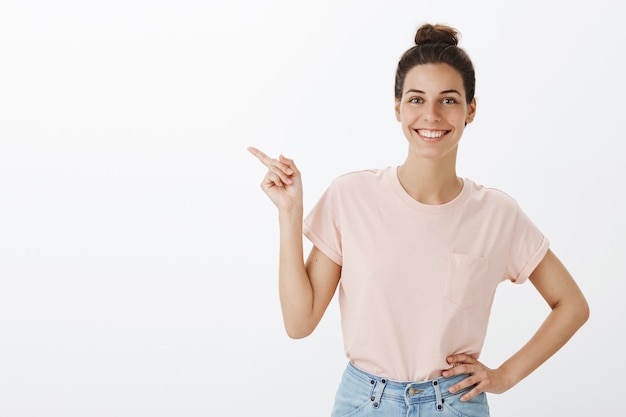 Attraente giovane donna alla moda sorridente in posa contro il muro bianco