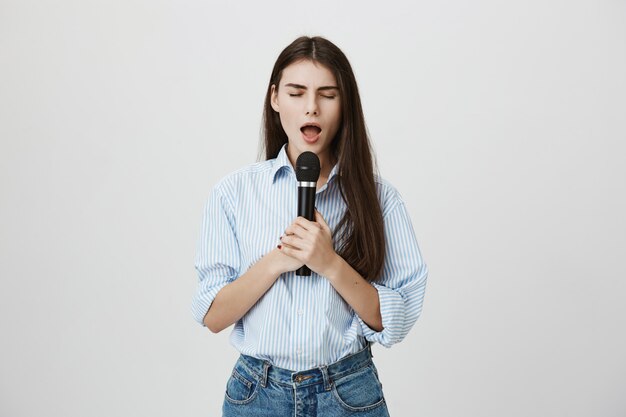 Attraente giovane donna che canta con gli occhi chiusi con il microfono