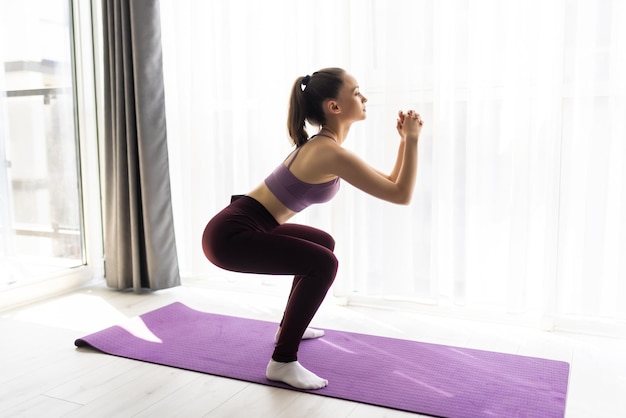 Attraente giovane donna in abbigliamento sportivo facendo sit-up in soggiorno, allenando le gambe, cercando di formare una perfetta forma di testa