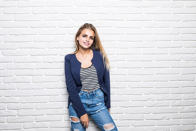 Attraente giovane donna in abiti casual alla ricerca e sorridente sul muro di mattoni bianchi