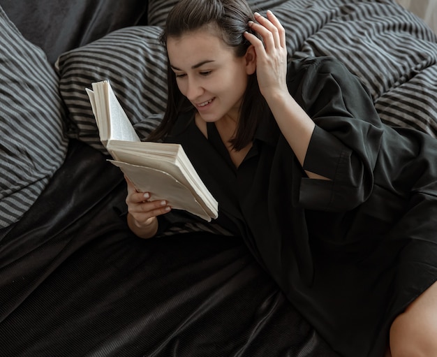 Attraente giovane donna in pigiama sta leggendo un libro mentre giaceva a letto.
