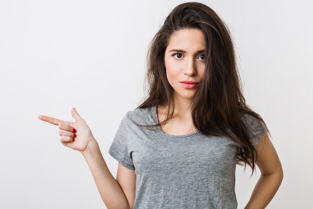 Attraente giovane donna in t-shirt grigia che punta il dito,, gesticolando