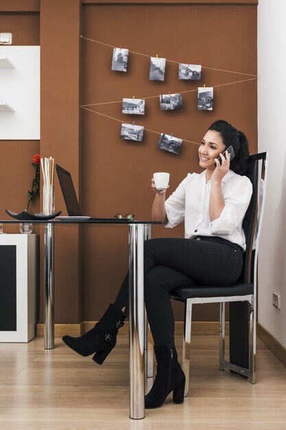 Attraente giovane imprenditrice che beve caffè e lavora in ufficio